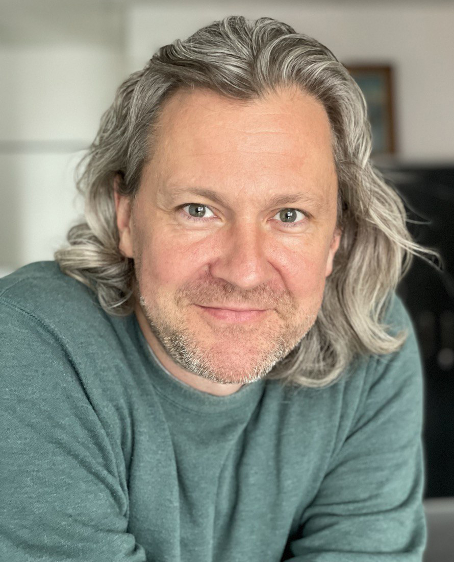 André Kramer smiling in a green  shirt and long grey hair